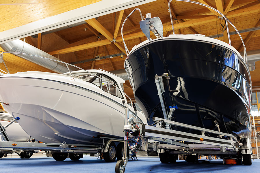 Two new boats on trailers inside a large storage facility or showroom with wooden beams overhead.